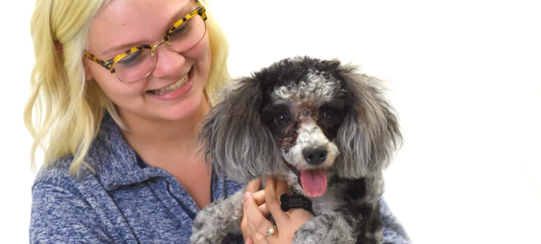 Blonde woman in glasses holding gray dog.